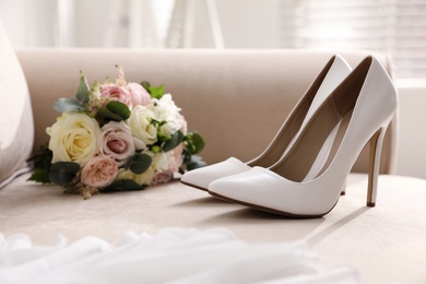 Photo of Pair of white wedding high heel shoes and beautiful bouquet on sofa indoors