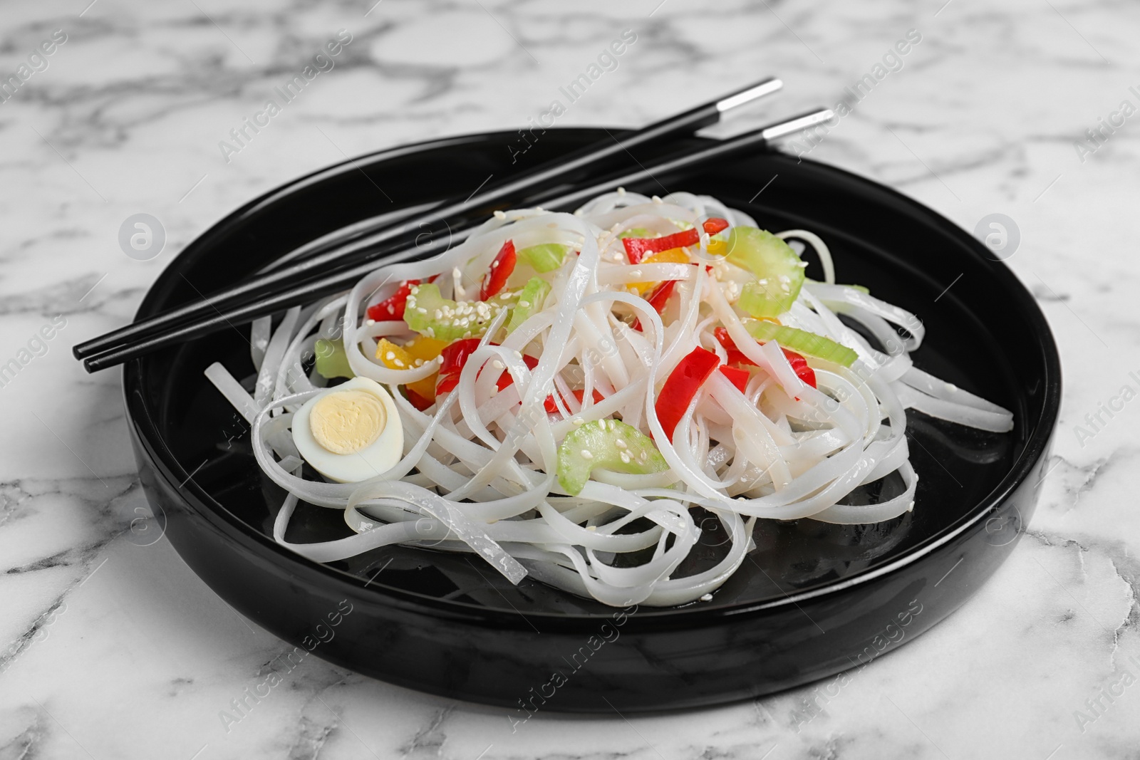 Photo of Plate of tasty noodles with chopsticks on marble table, closeup