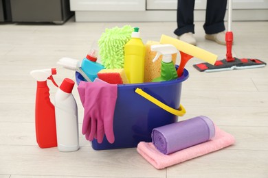 Photo of Different cleaning supplies in bucket and man mopping floor, selective focus