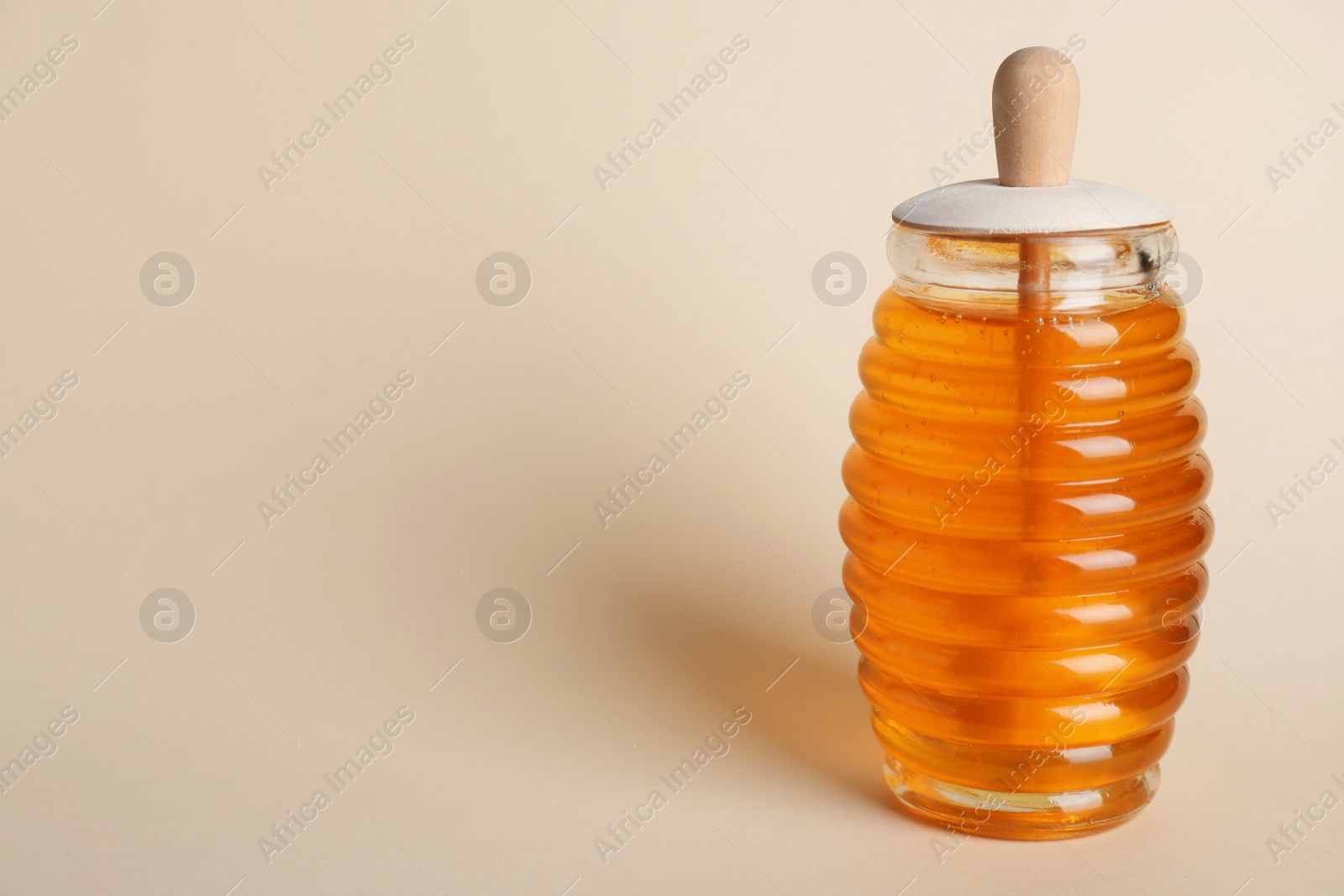 Photo of Jar of organic honey with dipper on beige background. Space for text