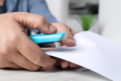 Photo of Man with papers using stapler at white table indoors, closeup