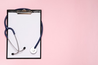 Stethoscope and clipboard on pink background, top view. Space for text