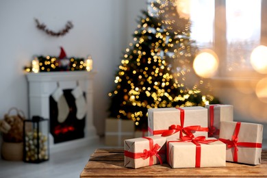 Photo of Many different gift boxes on wooden table against blurred festive lights in living room, space for text. Christmas presents