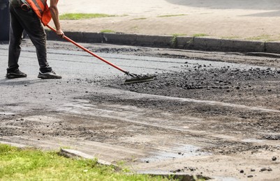 Photo of Worker laying new asphalt on city street, closeup. Road repair service