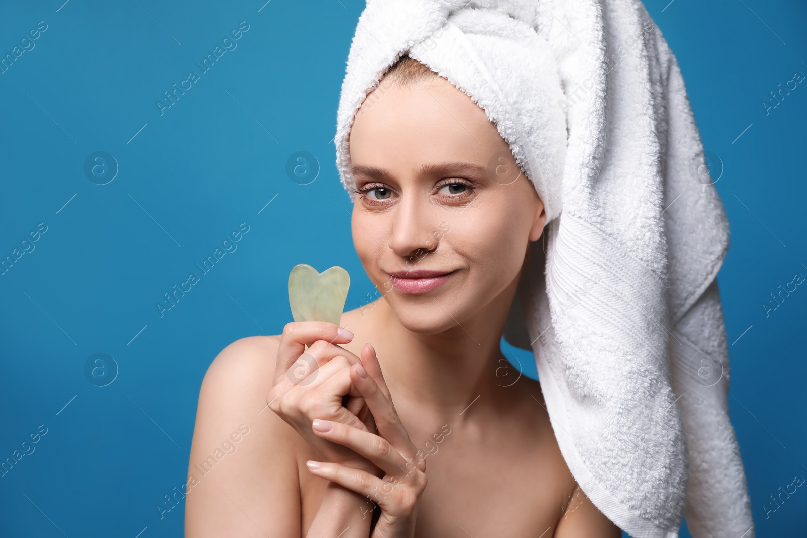 Photo of Beautiful young woman doing facial massage with gua sha tool on blue background