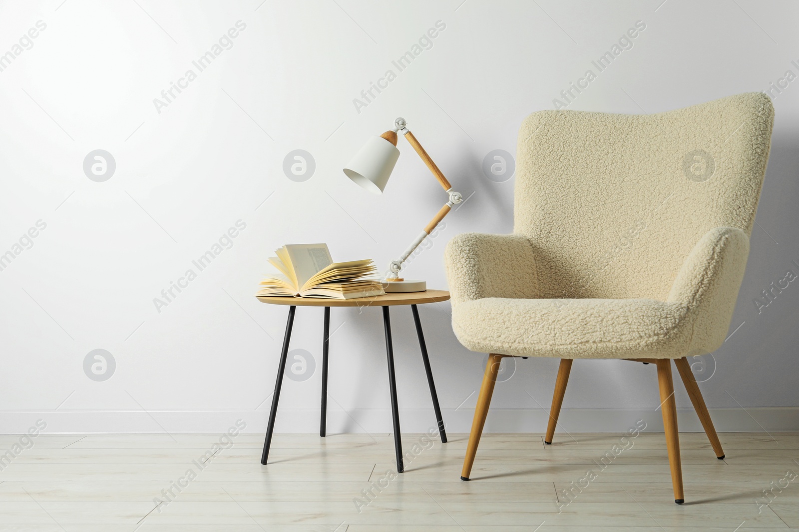 Photo of Stylish lamp with open book on wooden coffee table and soft armchair in light room. Interior design