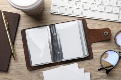 Leather business card holder with blank cards, stationery and keyboard on wooden table, flat lay