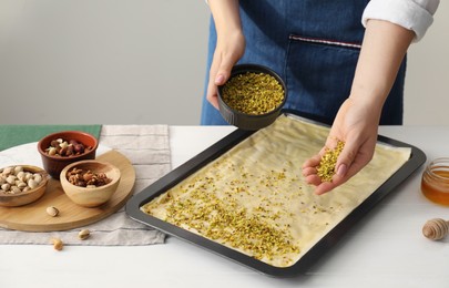 Making delicious baklava. Woman adding chopped nuts to dough at white wooden table, closeup. Space for text