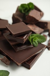 Photo of Tasty dark chocolate pieces with mint on white background, closeup