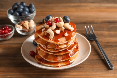 Stack of tasty pancakes with berries, nuts and syrup on table