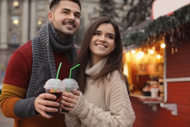 Young couple with cups of mulled wine at winter fair