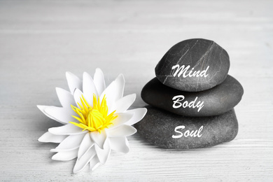 Photo of Stones with words Mind, Body, Soul and lotus flower on white wooden table. Zen lifestyle