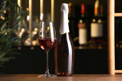 Photo of Bottle and glass of delicious rose wine on wooden table in bar