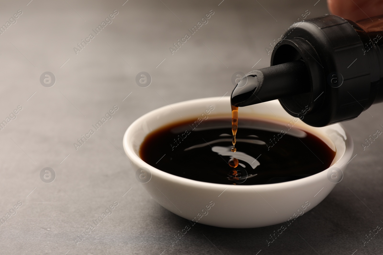 Photo of Pouring soy sauce into bowl on grey table, closeup. Space for text