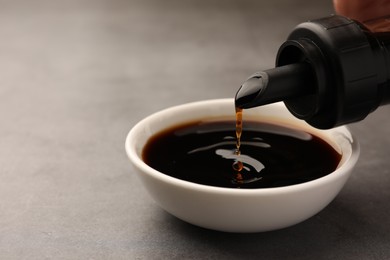 Pouring soy sauce into bowl on grey table, closeup. Space for text