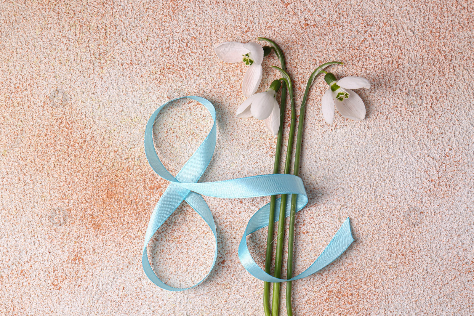 Photo of Beautiful snowdrops and number 8 made of ribbon on color textured background, flat lay