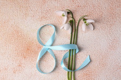 Photo of Beautiful snowdrops and number 8 made of ribbon on color textured background, flat lay