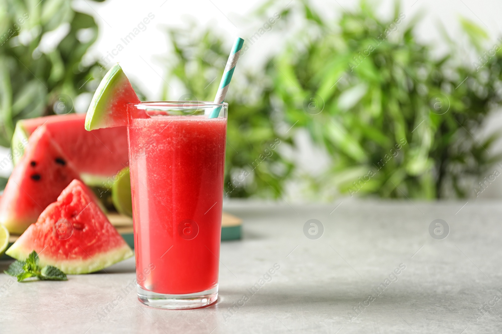 Photo of Tasty summer watermelon drink in glass on table against blurred background. Space for text