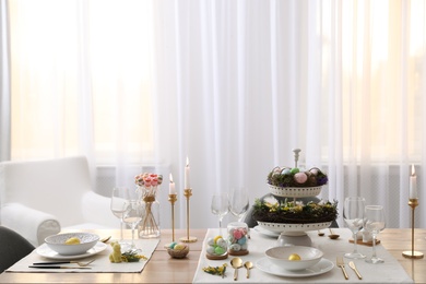 Beautiful Easter table setting with burning candles and floral decor indoors