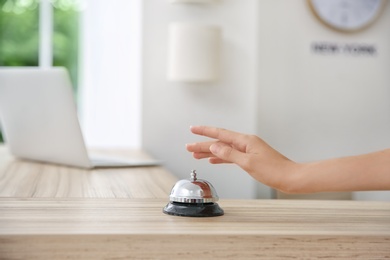 Photo of Woman ringing service bell on reception desk in hotel, closeup