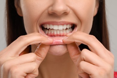 Photo of Woman showing her clean teeth on light grey background, closeup