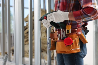 Photo of Professional builder with tool belt and power drill indoors, closeup