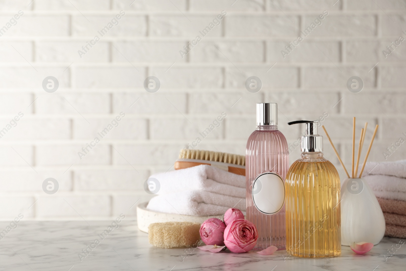 Photo of Stylish dispenser with liquid soap and other bathroom amenities on white marble table, space for text