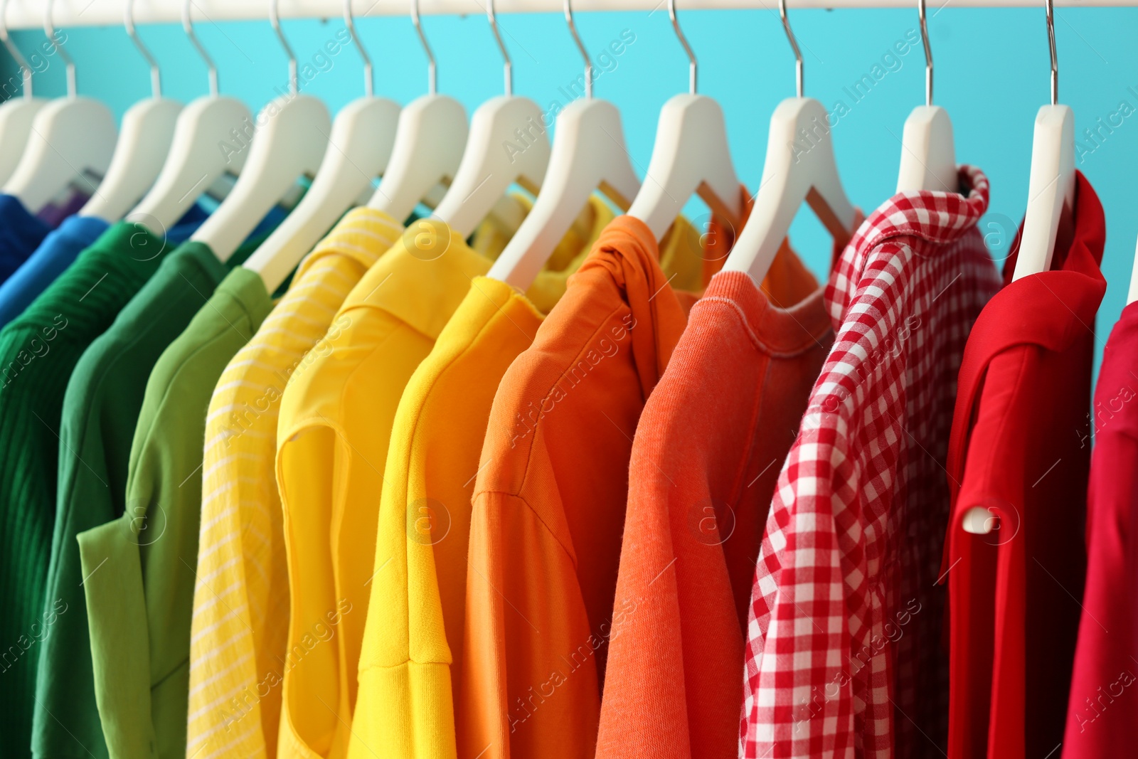 Photo of Rack with rainbow clothes on color background