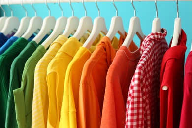 Photo of Rack with rainbow clothes on color background