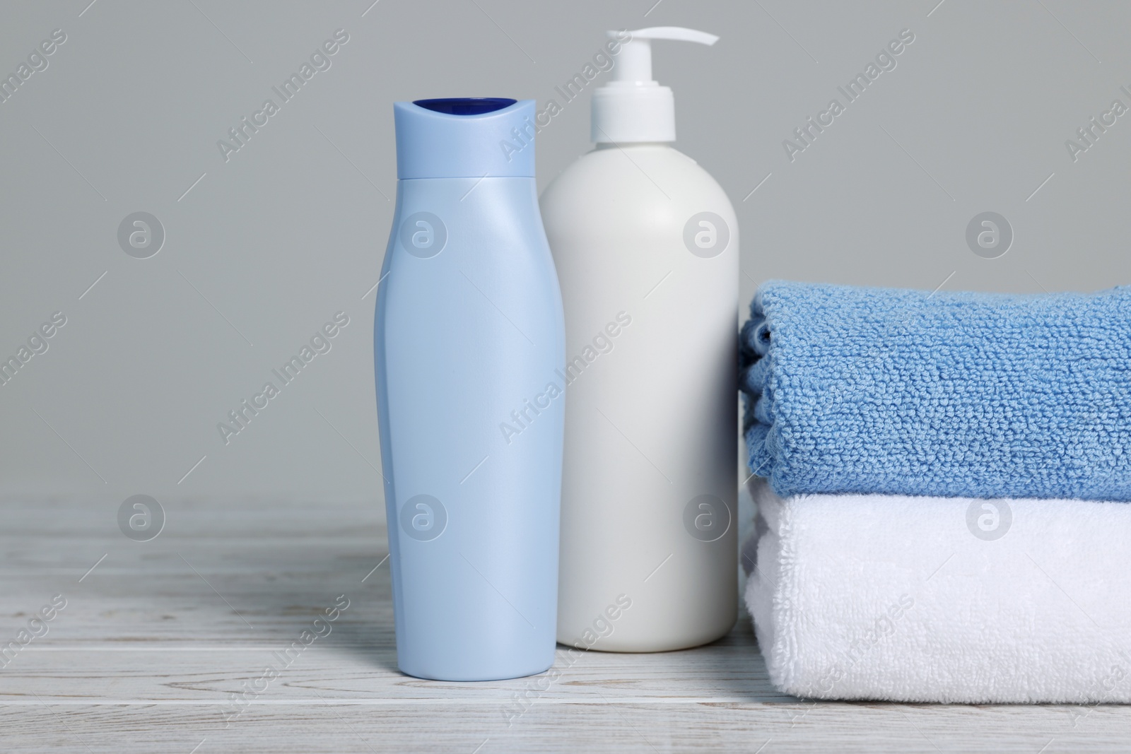 Photo of Soft folded towels with cosmetic products on white wooden table against light grey background