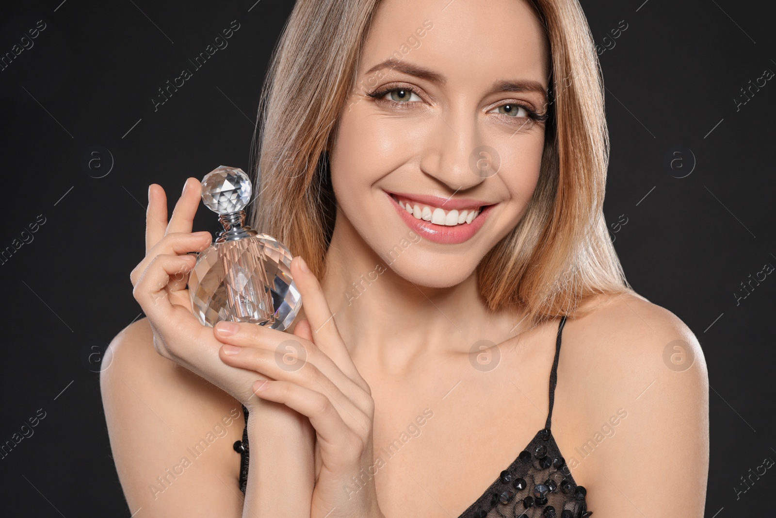 Photo of Young woman with bottle of perfume on black background