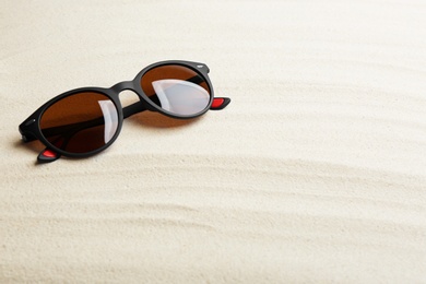 Stylish sunglasses on white sand, space for text. Summer time