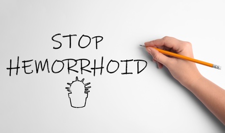 Image of Woman writing phrase STOP HEMORRHOID on white background, top view