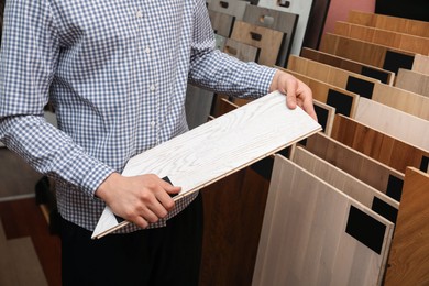 Photo of Man with sample of light wooden flooring in shop, closeup