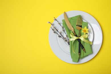 Festive table setting with willow twigs and space for text on yellow background, top view. Easter celebration