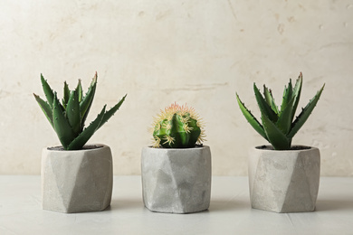 Photo of Artificial plants in cement flower pots on table against light background