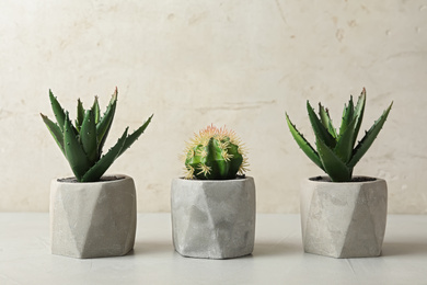 Artificial plants in cement flower pots on table against light background