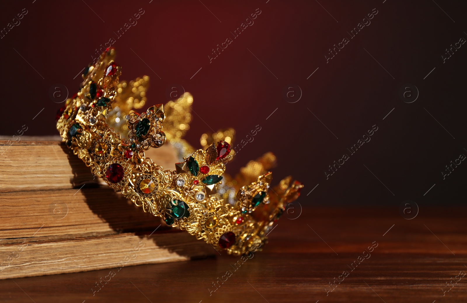 Photo of Beautiful golden crown and old books on wooden table, space for text. Fantasy item