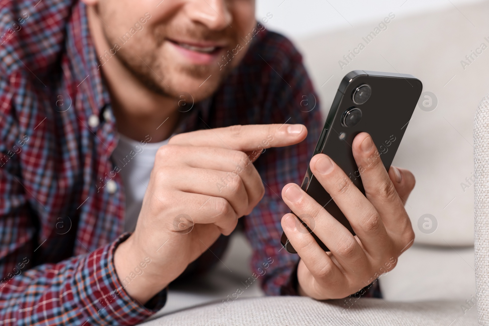 Photo of Man sending message via smartphone on sofa indoors, closeup