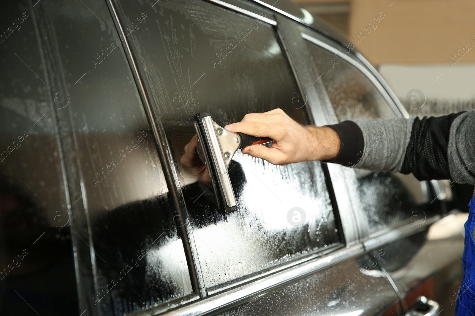 Photo of Worker washing tinted car window in shop, closeup