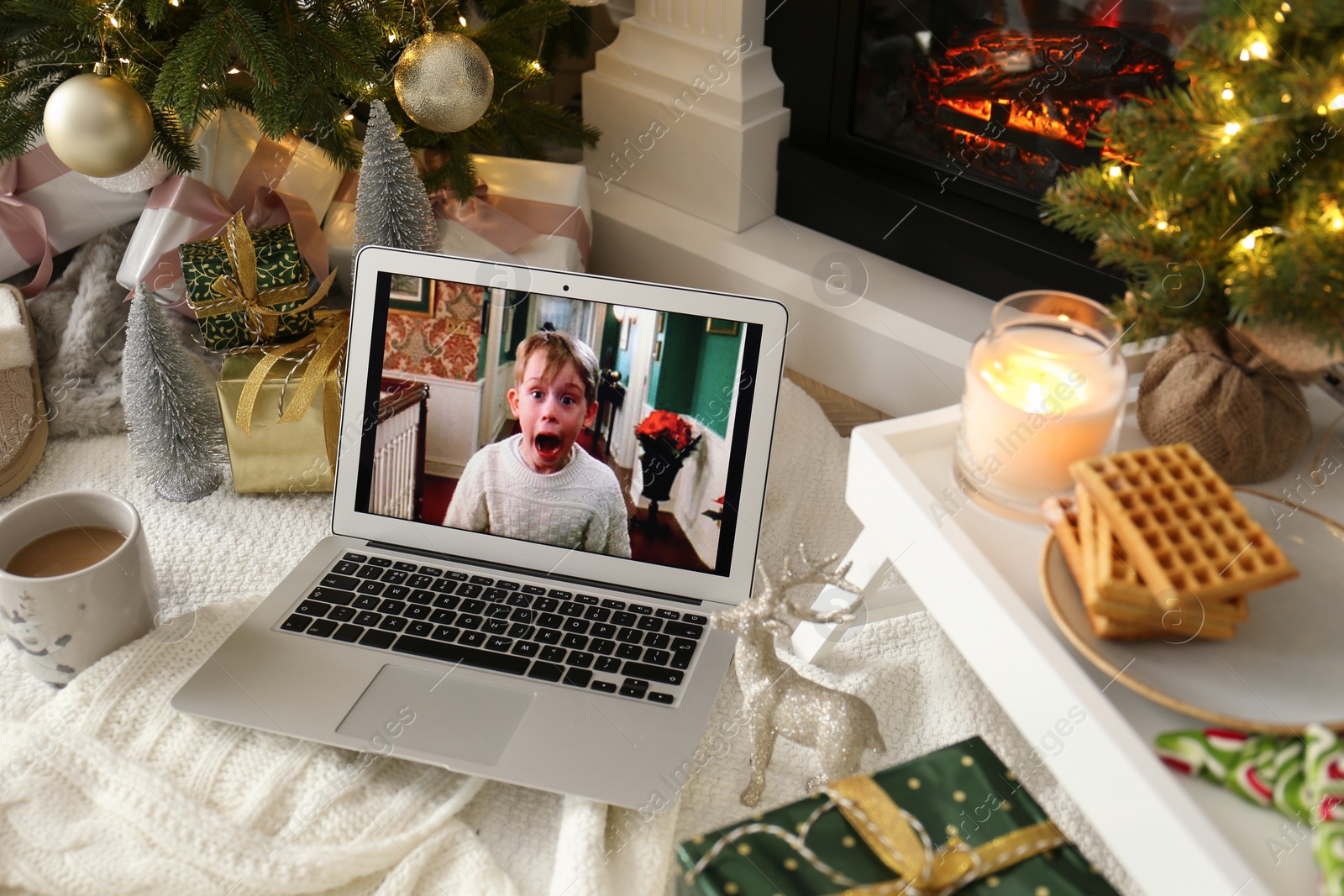 Photo of MYKOLAIV, UKRAINE - DECEMBER 23, 2020: Laptop displaying Home Alone movie near fireplace indoors. Cozy winter holidays atmosphere