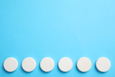 Photo of White pills on light blue background, flat lay. Space for text