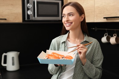 Beautiful young woman eating sushi rolls with chopsticks in kitchen