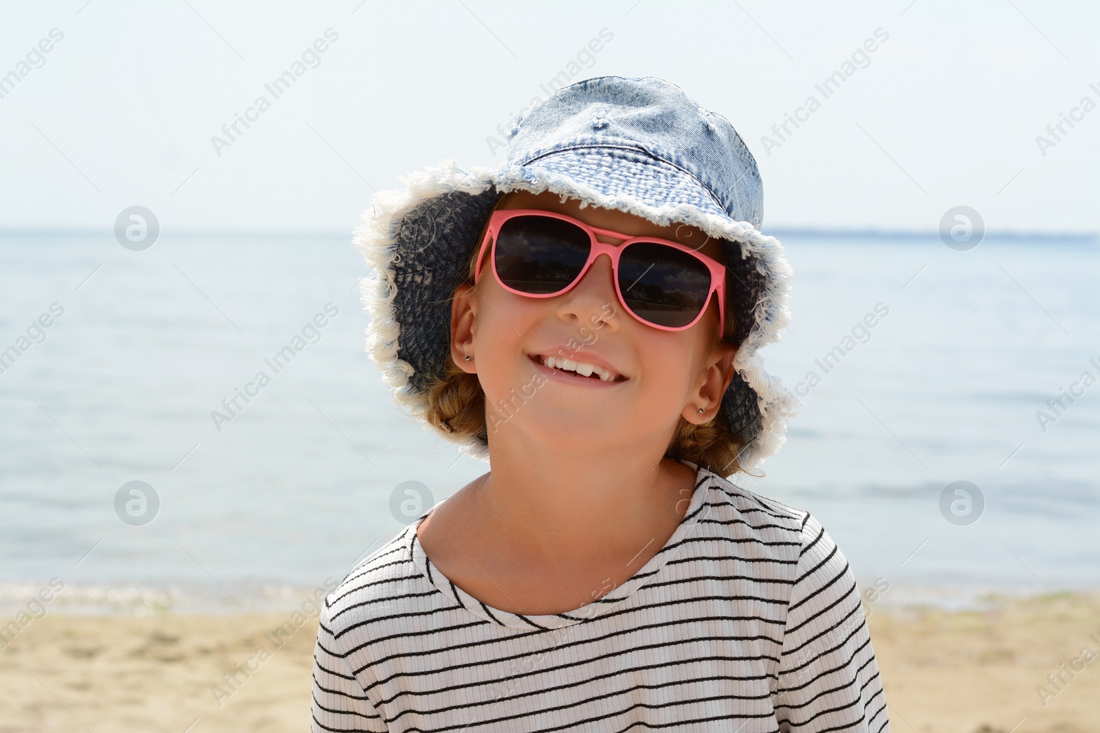 Photo of Little girl wearing sunglasses and hat at beach on sunny day