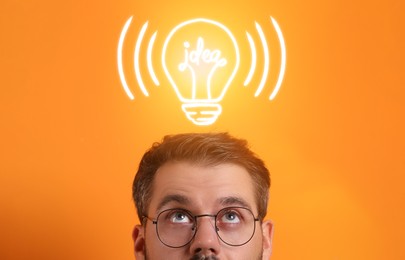 Image of Idea generation. Man looking at illustration of glowing light bulb over him on orange background