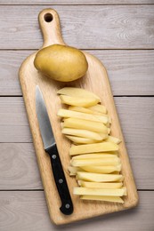 Whole and cut raw potatoes with knife on wooden table, top view