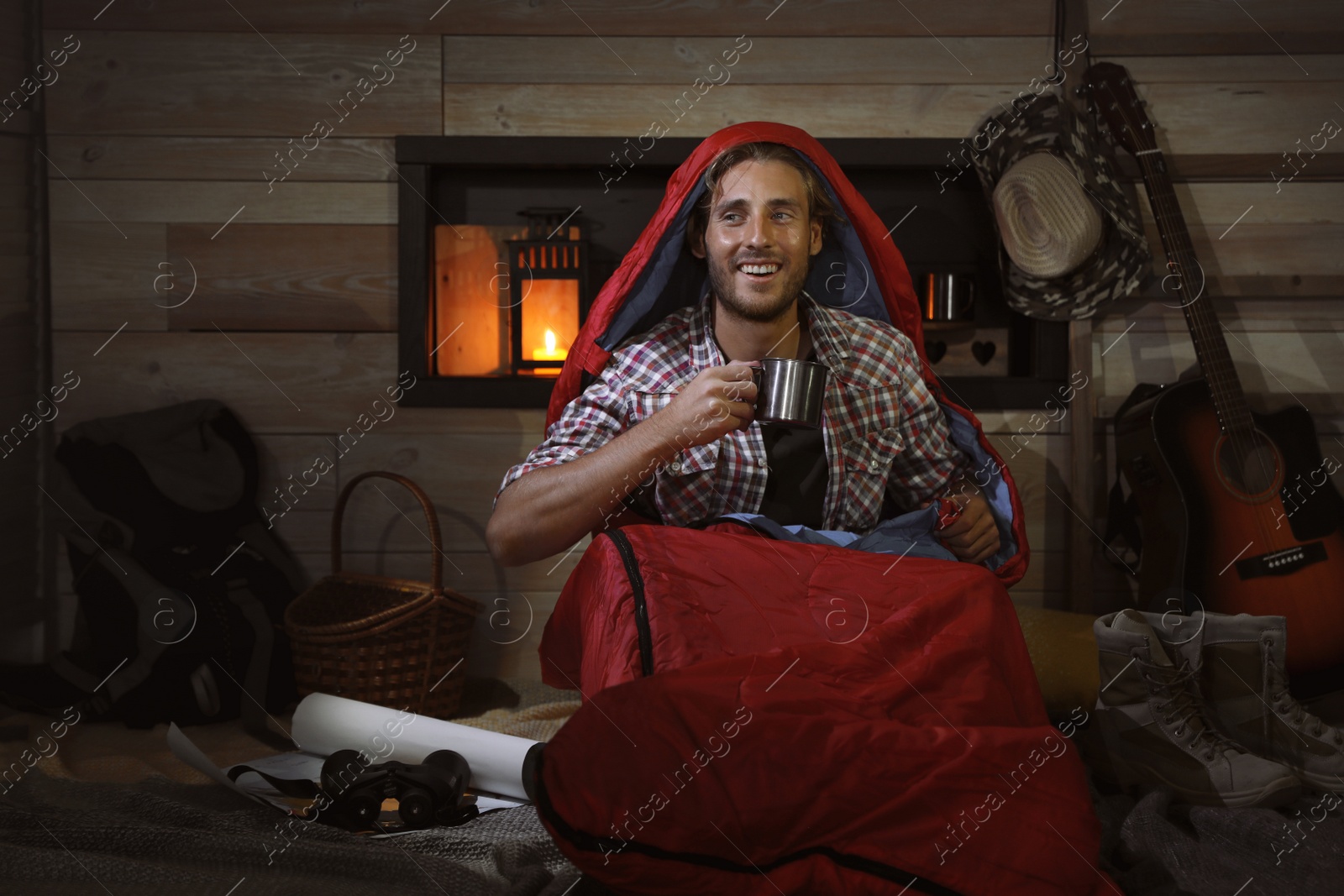 Photo of Young man in sleeping bag with mug indoors