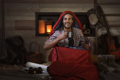 Young man in sleeping bag with mug indoors