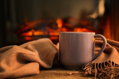 Cup with hot drink and blanket on table against fireplace