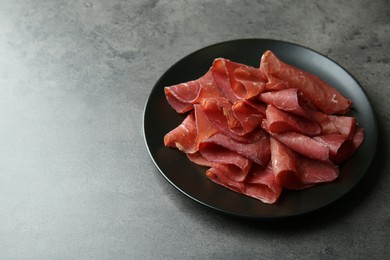 Photo of Plate with tasty bresaola on grey table. Space for text